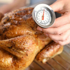 woman testing internal temperature of chicken with a meat thermometer 