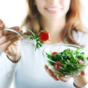 Woman holding a salad bowl and tomato on a fork 